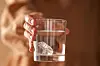 Närbild av en hand som håller ett glas vatten med en kristall i.