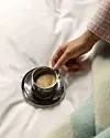 Hand rör om kaffe i en kopp på ett silverfat på en vit säng.