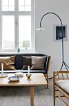 Ljust vardagsrum med soffa, soffbord, golvlampa och stora fönster.