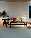 Ett vardagsrum med röd stol, soffbord, ljus, blommor och vit soffa mot ljus vägg.