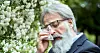 Äldre man i kavaj och glasögon torkar ögon med näsduk.