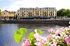 Stadshotellet i Karlstad är en gul byggnad precis intill vattnet, rosa blommor syns i förgrunden.
