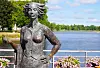 Staty i brons av kvinna vid blomsterprytt räcke intill vattnet.