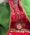 Närbild av röd folkdräkt med grönt ytterplagg och dekorativt halsband.