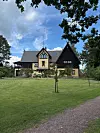 Gul och mörkbrun villa med människor på gräsmattan framför huset en sommardag.